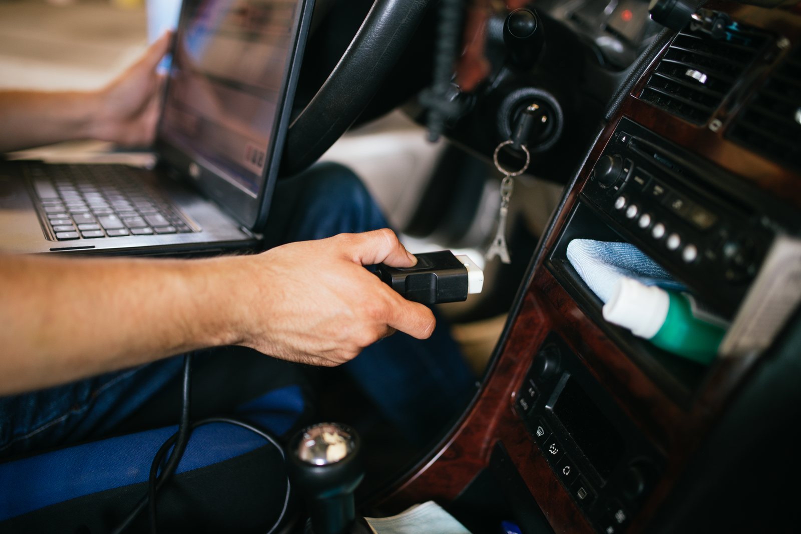 Technician connecting an unbranded OBD diagnostic cable inside a vehicle.