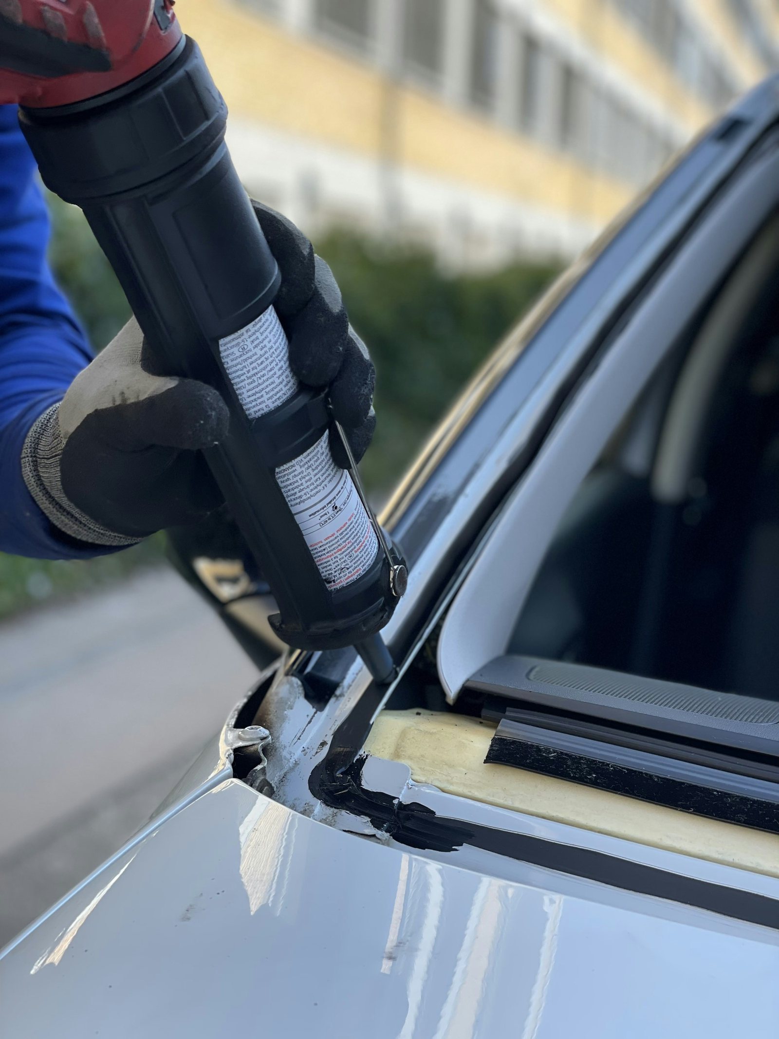 Gloved technician applying a controlled urethane bead along a windshield frame.