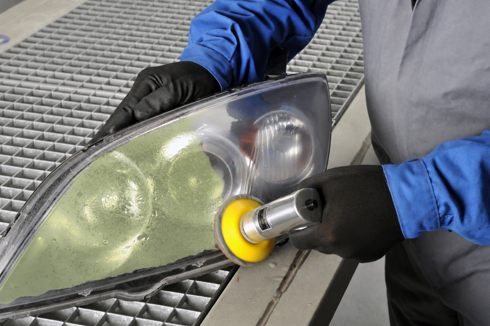 Technician wet-sanding the hazed surface of a detached headlight assembly on a workbench.