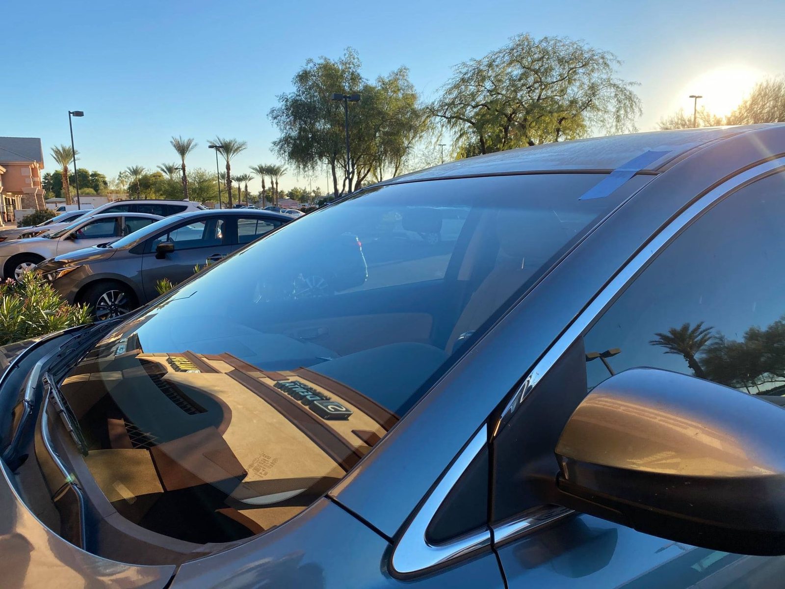 Completed windshield installation on a vehicle parked outdoors with retention tape in place.