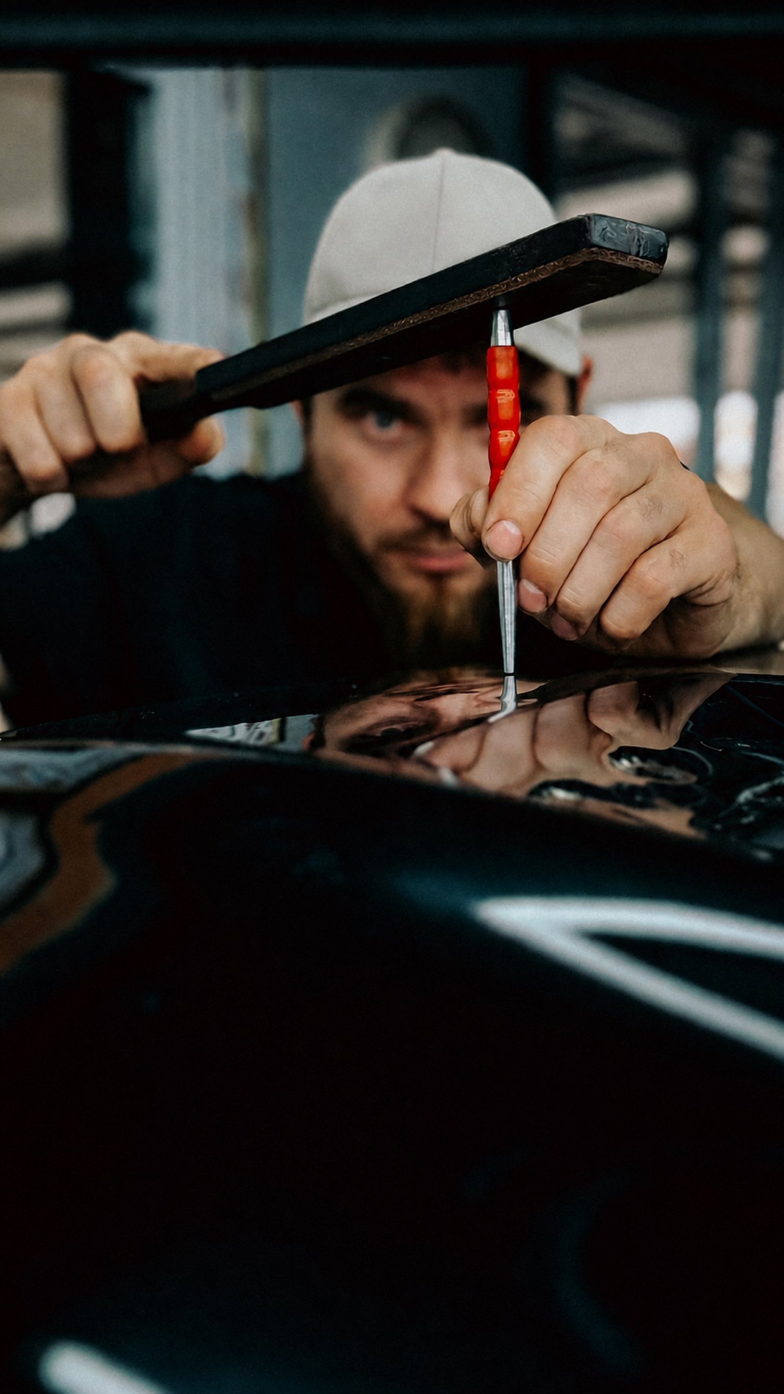 Paintless dent repair technician tapping down a high spot on an intact glossy black panel with a knockdown tool and hammer.