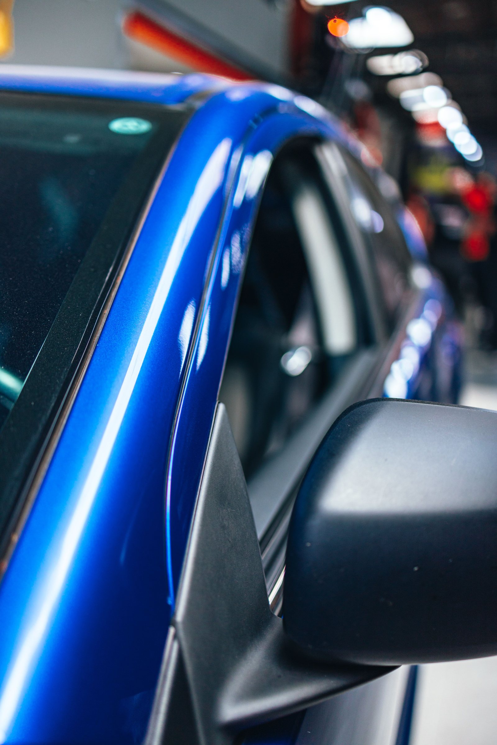 Glossy blue vehicle door and roof edge reflecting straight inspection lights in a clean workshop.