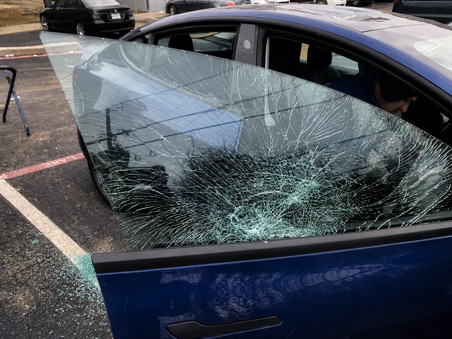 Severely damaged door glass being carefully removed from a blue vehicle.