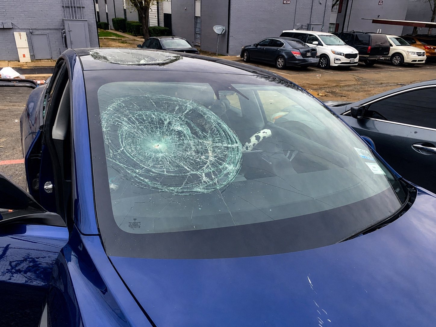 Blue vehicle with severe windshield impact damage before replacement.